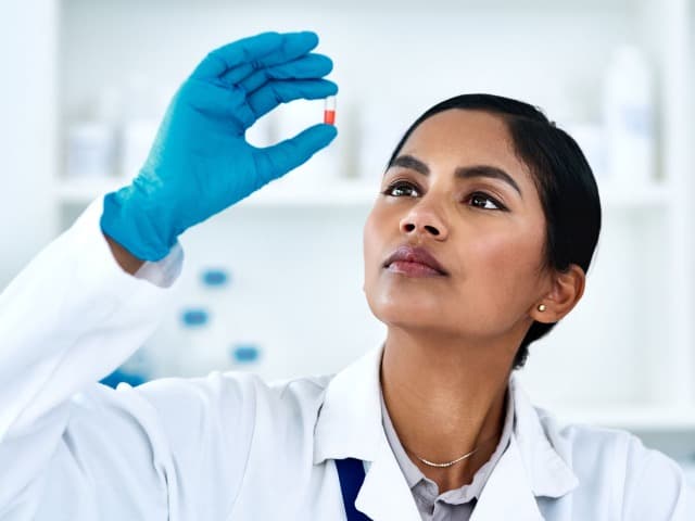 Element scientist in white coat and safety goggles in life sciences testing laboratory interacting with advanced analytical equipment for pharmaceutical research